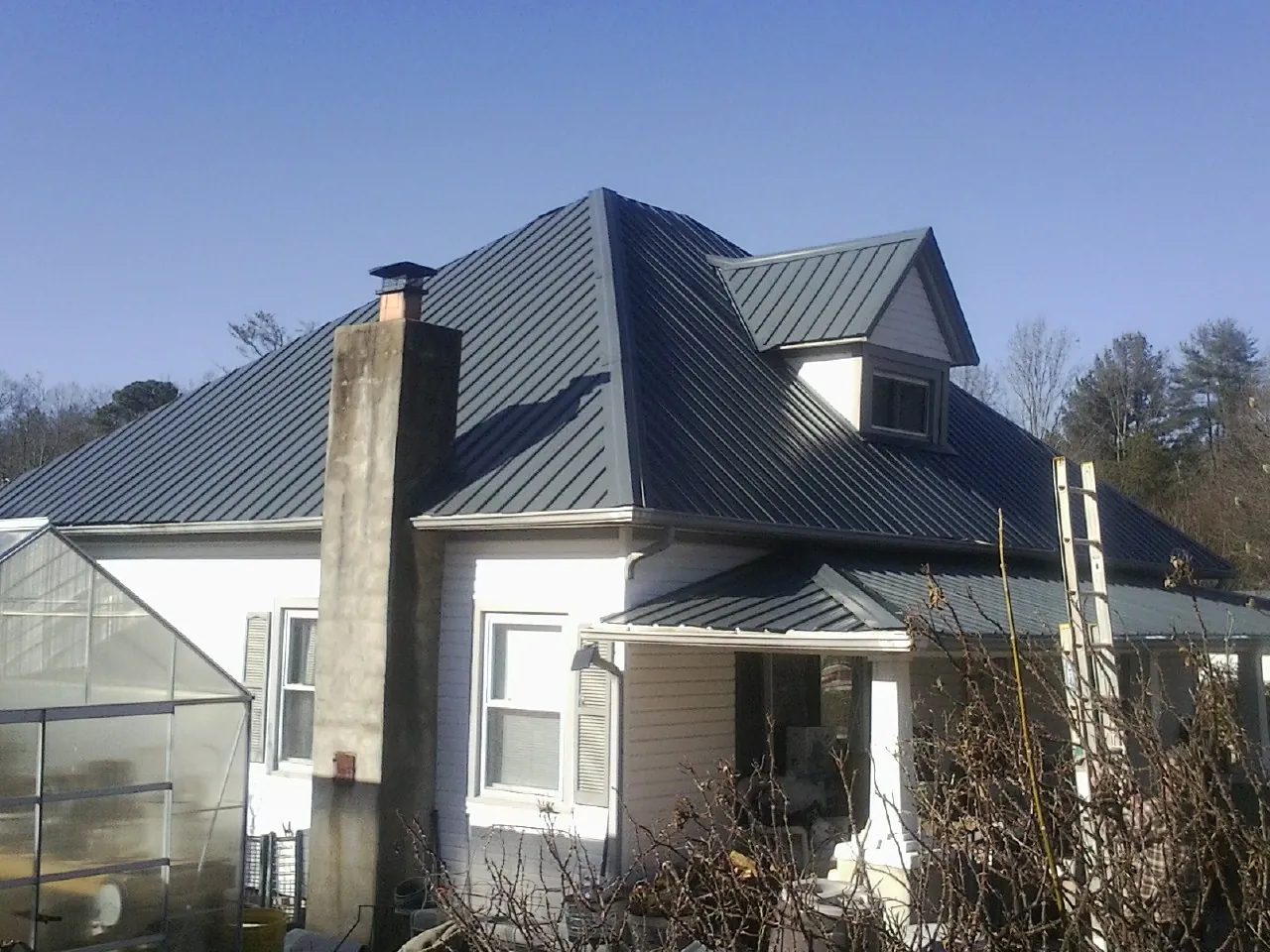 Dark blue standing seam metal roof on a white farmhouse with dormer — Slate & Tile Roof Repair by Roofing Brothers in Grand Haven