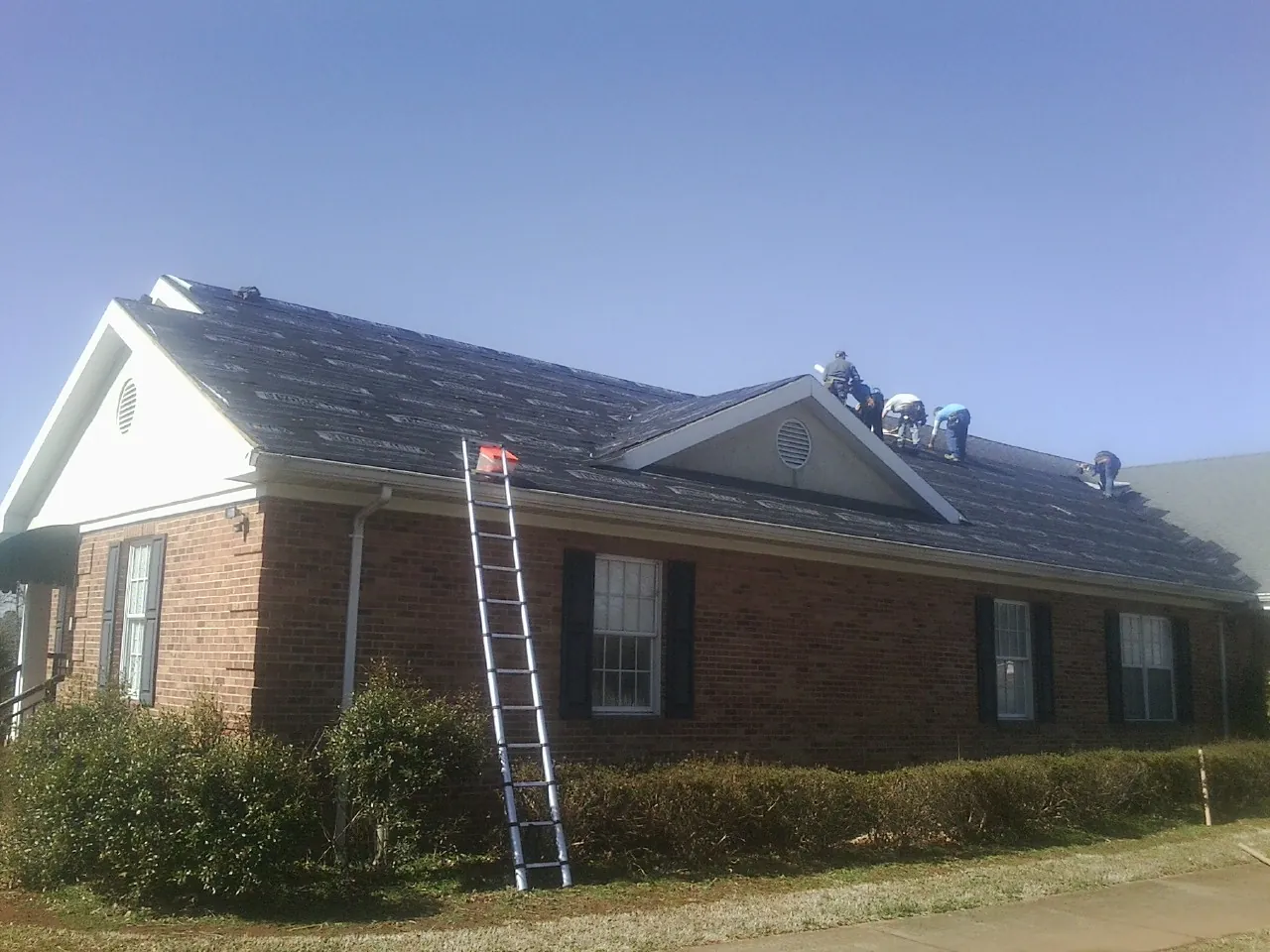 Crew tearing shingles off a brick ranch roof with a ladder set — Metal Roof Repair work by our crew in Grand Haven