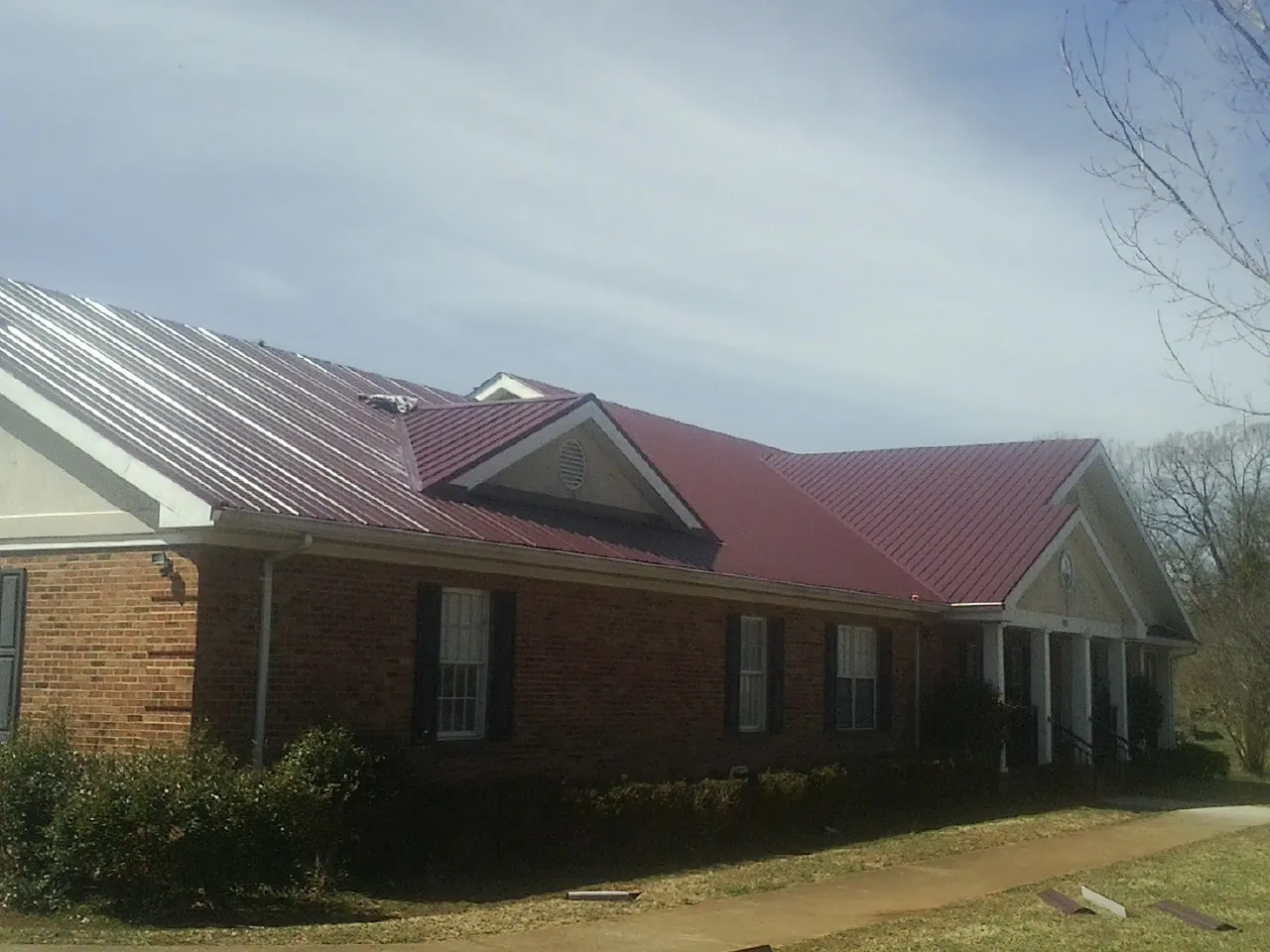 Red metal roof with gabled entries on a long brick building, from a Hail Damage Roof Repair job in Grand Haven