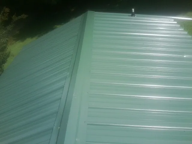 New green metal panels meeting at the ridge of a roof — Flat Roof Repair work by our crew in Grand Haven