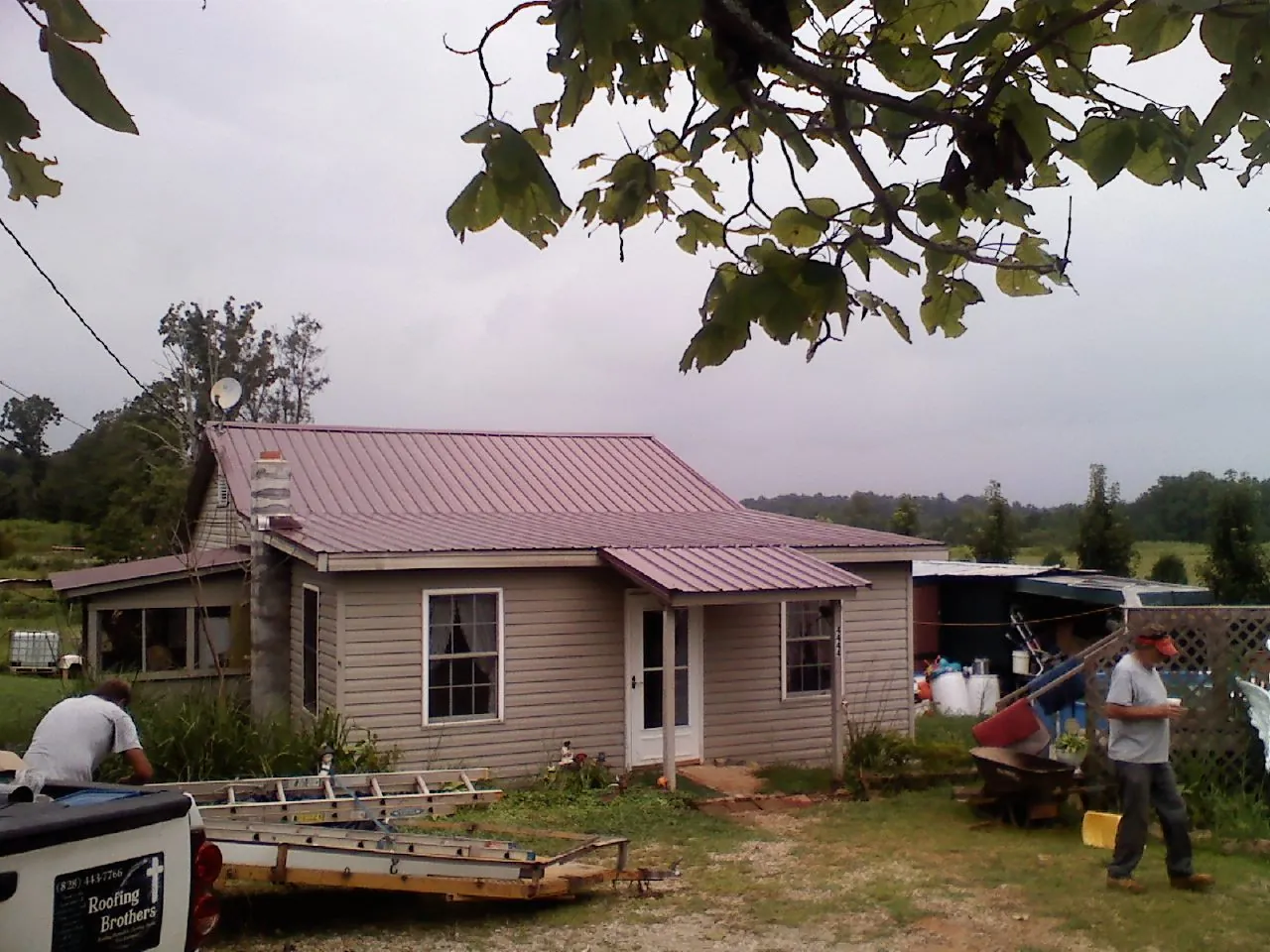 Crew finishing a mauve metal roof on a small farmhouse in Grand Haven