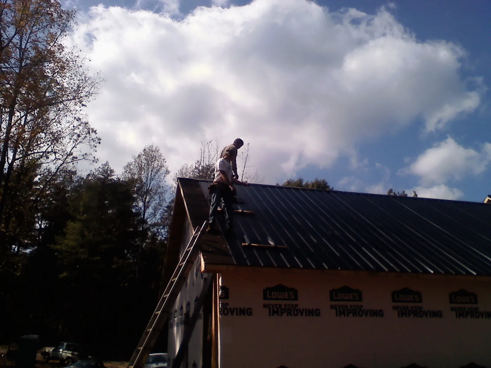 Roofer fastening dark metal panels high against a cloudy sky, from a Roof Inspection job in Grand Haven