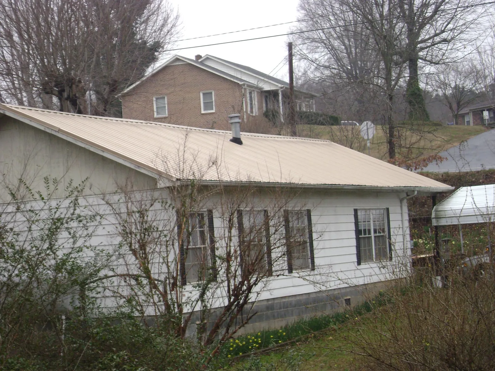 Tan metal roof on a white sided house set into a hillside — Commercial Roofing by Roofing Brothers in Grand Haven