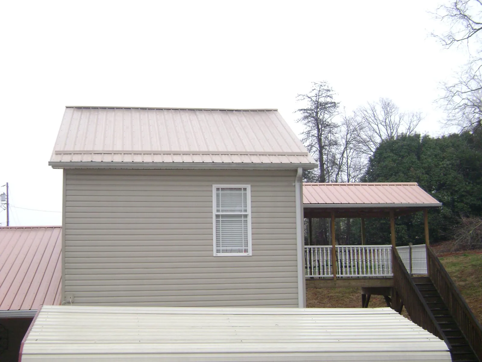 Tan metal roofs on a two story addition and attached porch, from a Roof Replacement job in Grand Haven